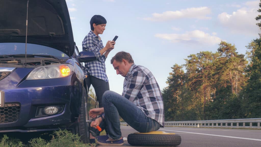 HeartBeep Marketing NH Intent Based Marketing, man changing a tire on the side of the road. Woman using mobile phone messaging or scrolling social media on smartphone