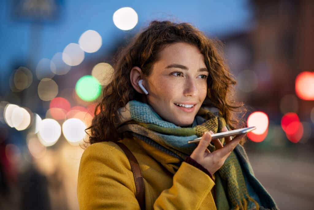 HeartBeep Marketing NH Intent Based Marketing, Happy woman recording message using voice on smartphone. Happy woman recording audio on mobile phone in the street at evening. Smiling woman speaking on her smart phone in winter evening.
