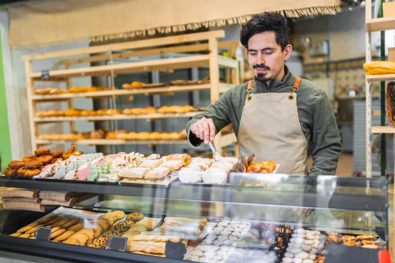 HeartBeep Marketing NH marketing in New Hampshire, Baker using tongs to arrange delicious pastries in a display case at a bakery shop, showcasing a variety of baked goods