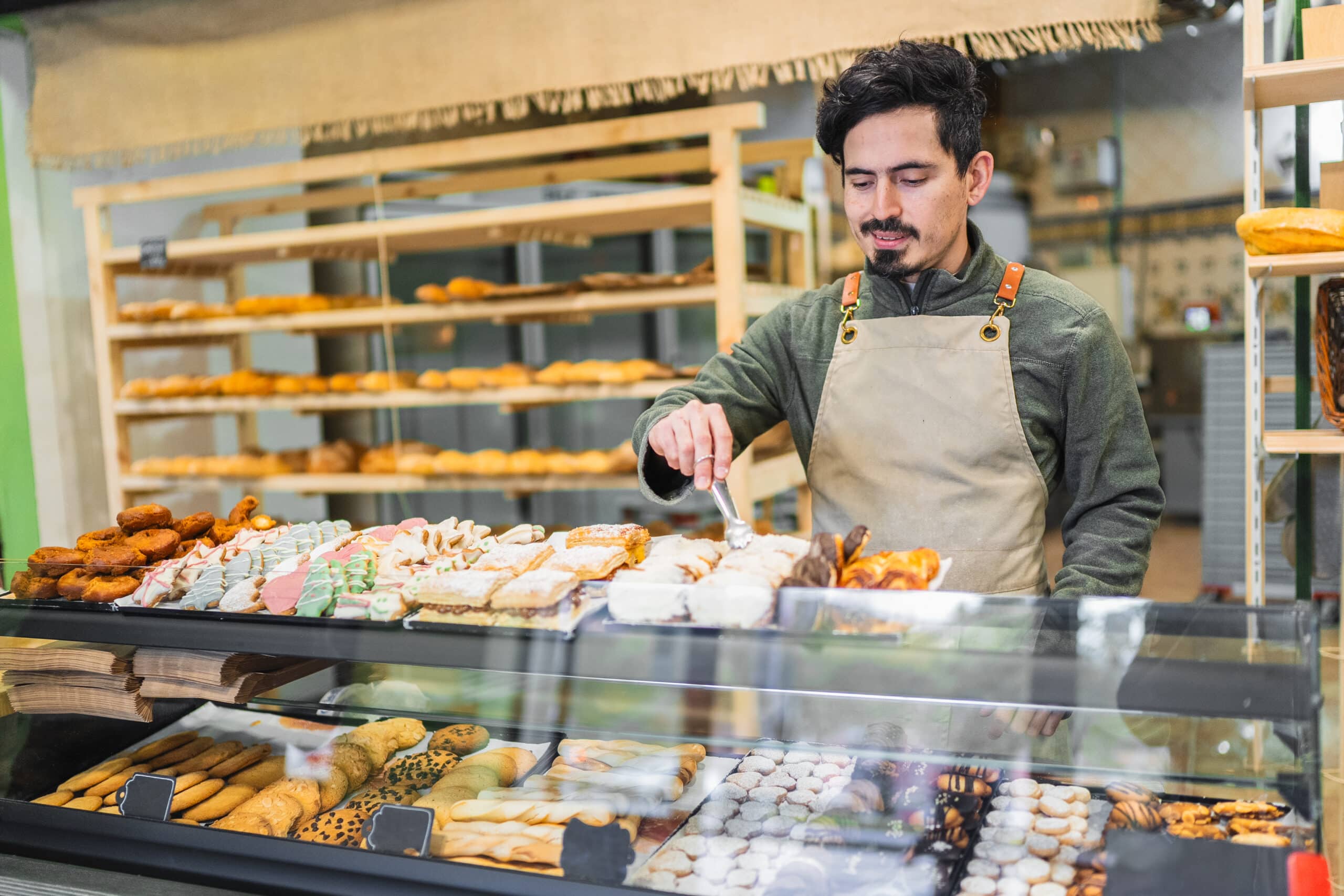 HeartBeep Marketing NH marketing in New Hampshire, Baker using tongs to arrange delicious pastries in a display case at a bakery shop, showcasing a variety of baked goods